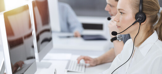 Call center. Group of casual dressed operators at work. Blond business woman in headset at customer...