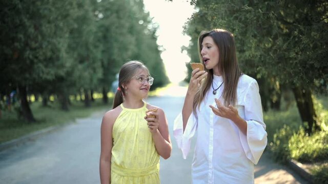 Woman with daughter funny eating ice cream outdoors. Funny children walking. Woman with daughter teenager indulging with ice cream