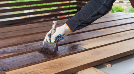 Brown color stain painting on wooden table or fence or wall, or flour, use for home decorated. House renovation. Half - painted surface. Hand holding brush. Background with copy space.