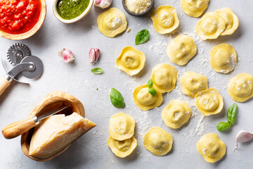 Fresh ravioli with pesto sauce, tomato sauce, Parmesan cheese, Basil on a light grey background. Top view.