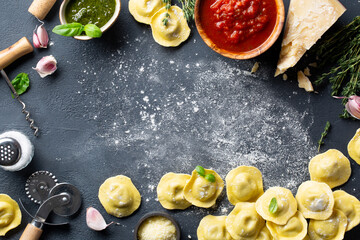 Fresh ravioli with pesto sauce, tomato sauce, Parmesan cheese, Basil on a dark background. Top view.