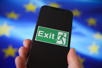 Viersen, Germany - July 9. 2020: View on isolated mobile phone screen with green emergency evacuation exit sign. Blurred  european flag background.
