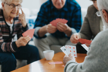 Senior friends sit at a coffee table and play cards
