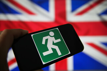 Viersen, Germany - July 9. 2020: View on isolated mobile phone screen with green emergency evacuation exit sign. Blurred union jack background.