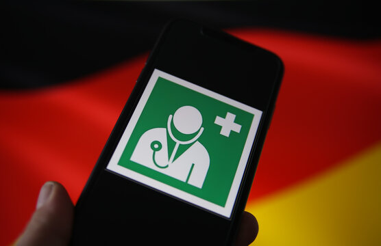 Viersen, Germany - July 9. 2020: View on isolated mobile phone screen with international health and medical doctor symbol. Blurred waving german flag background. (Focus on head of doctors symbol)
