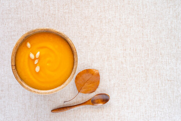 Pumpkin soup in wooden bowl with pumpkin seeds on cotton fabric background with copy space. Thanksgiving food. Halloween meal. Vegetarian soup.