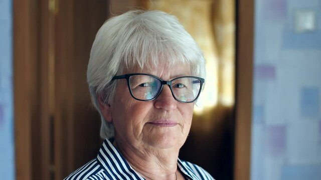 Portrait of an elderly gray-haired woman in stylish glasses, looking at the camera with a twist. Stylish old woman face and eyes with glasses
