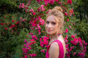 Fototapeta premium blonde with curly hair and beautiful makeup in a dress on a background of blooming roses