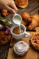 Assorted pastries, croissants, buns. On a brown wooden table.
