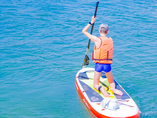 a young rider on a board for Sap surfing rakes a wave with a paddle, the concept of an active...