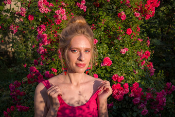 blonde with curly hair and beautiful makeup in a dress on a background of blooming roses