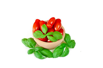 Tomatoes in a wooden bowl on a white background surrounded by basil