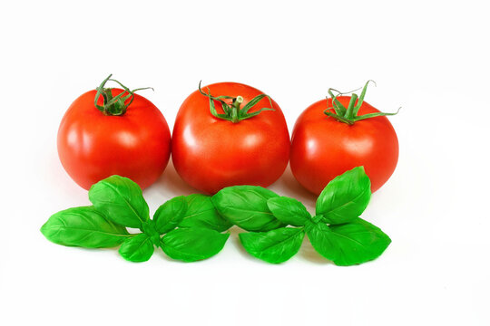 Dojrzałe, czerwone pomidory otoczone liśćmi bazylii na białym tle