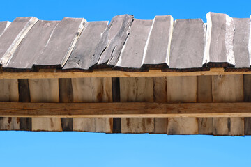 Part of narrow wooden roof against a blue sky. Such narrow wooden roofs are used for decoration above the entrance, such as gates