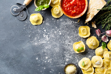 Fresh ravioli with pesto sauce, tomato sauce, Parmesan cheese, Basil on a dark background. Top view. Space for text.