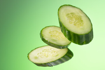 Three pieces of cucumber hang arbitrarily on a green background with a gradient.