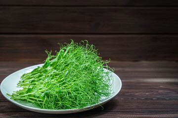 fresh cutted pea microgreen sprouts on plate on wooden surface.