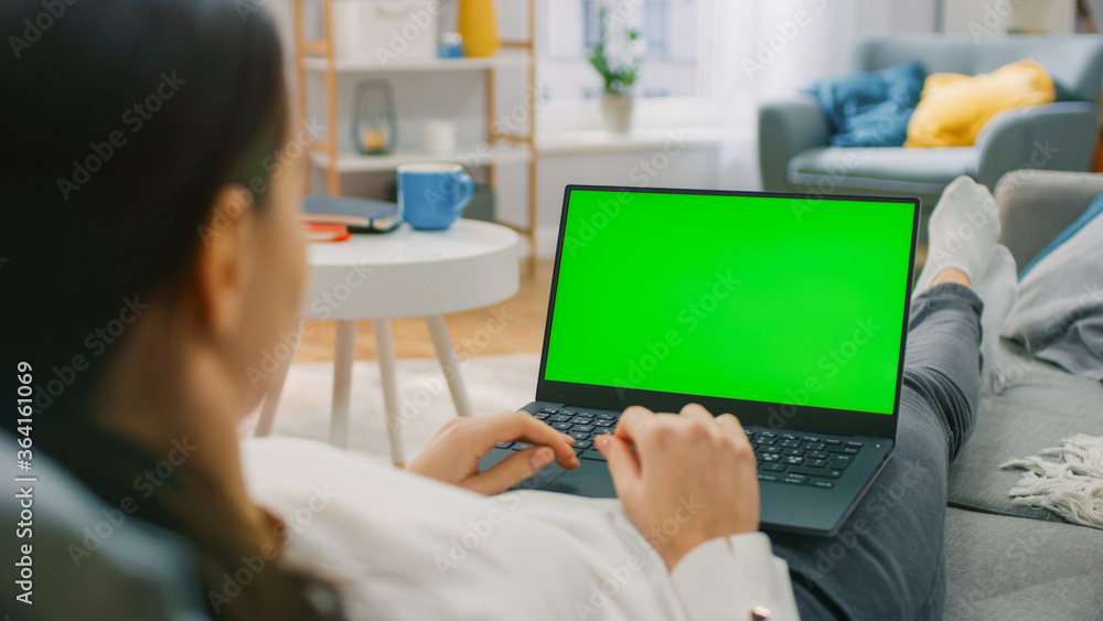 Poster woman at home lying on a couch working on laptop computer with green mock-up screen. girl using comp