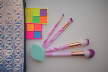 a set of five bright cosmetic brushes white with pink with two sponges and a set of bright eye shadows and a cosmetic bag on a white background top view