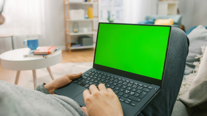 Man at Home Laying on a Couch Using with Green Mock-up Screen Laptop Computer. Guy Using Laptop...