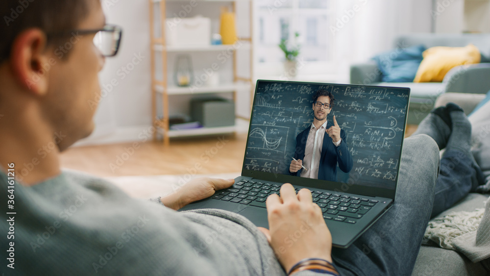 Poster man at home sitting on a couch using laptop computer for video call to his teacher. screen shows onl