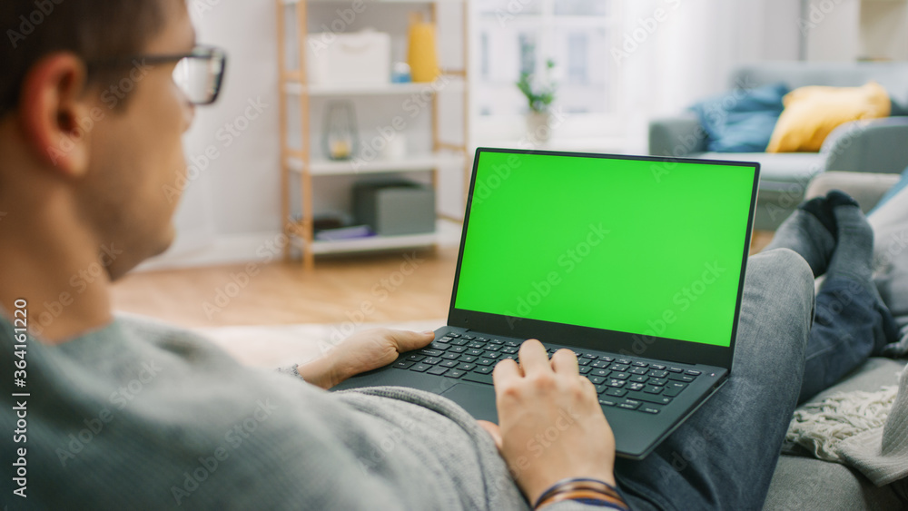 Poster man at home sitting on a couch working on green mock-up screen laptop computer. guy using laptop dev