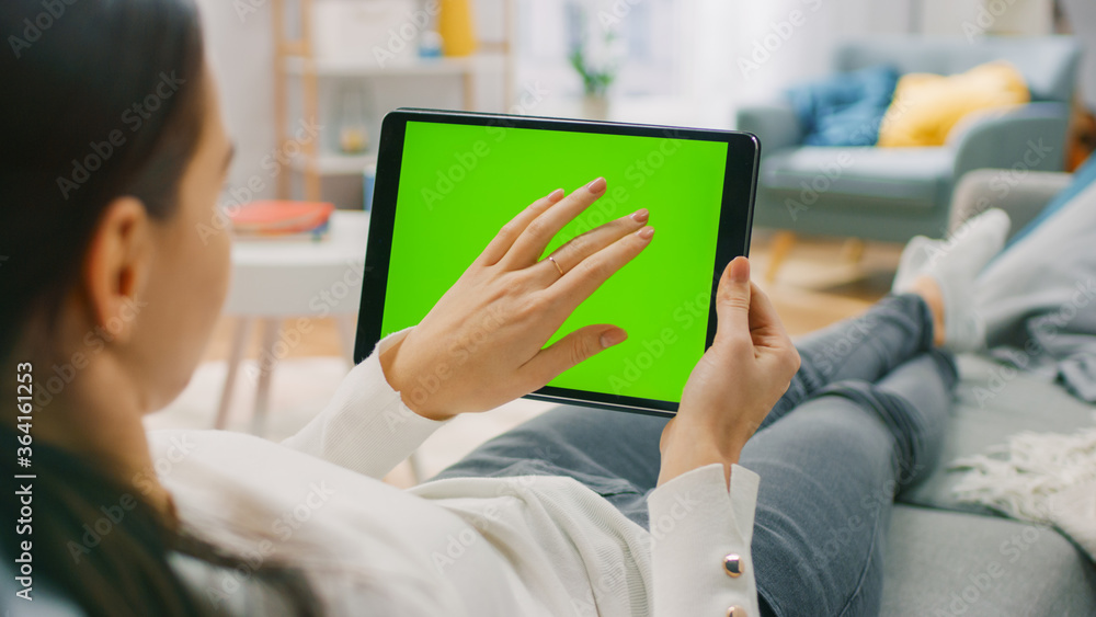Poster young woman at home resting on a couch using with green mock-up screen tablet computer in horizontal