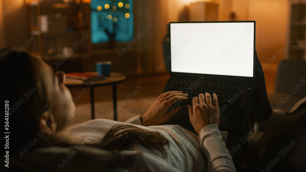 Poster evening at home: young woman resting on a couch using with white mock-up screen laptop computer. gir