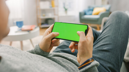Man at Home Lying on a Couch using Smartphone, Holds it Horizontally in Landscape Mode. Pushing...