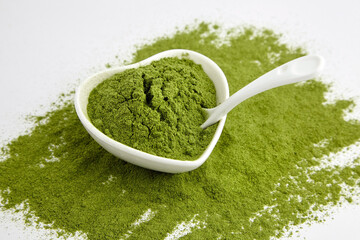 Green freeze dried wheat or barley grass powder in ceramic bowl with spoon on white.