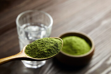 Wheatgrass or barley grass powder in spoon and glass of water. Detox juice preparation.