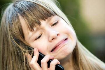 Portrait of stressed child girl with long hair talking on cell phone. Little female kid communicating using smartphone. Children communication concept.