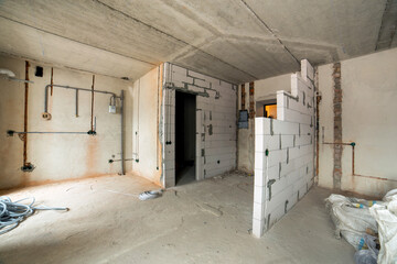 Interior of an apartment room with bare walls and ceiling under construction.