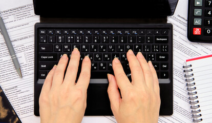 Man's hands type on laptop keyboard near calculator and notepad with pen