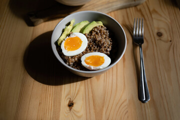 Buckwheat with boiled eggs and fresh green avocado in the bowl. Lunch at the wooden table with a fork
