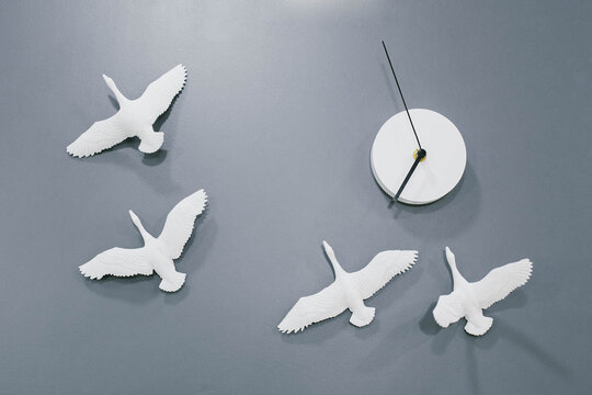 Modern simple white wallclock with birds pattern on grey background.