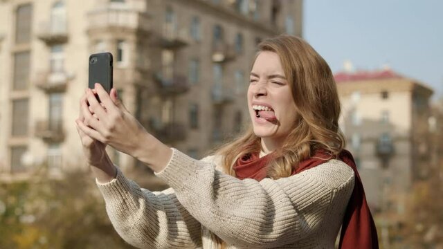 Pretty girl making selfie photo outdoors. Funny woman using cellphone on street.