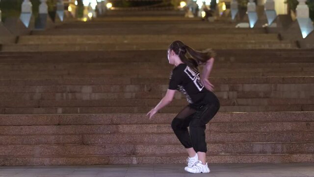 Beautiful young girl in leopard t-shirt dancing street dance outdoors in front of an old huge stone staircase in night. Urban dancing freestyle in the city
