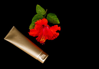 Golden cream bottle and tropical flower on the black background.