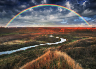 Amazing rainbow over the small rural river. autumn morning

