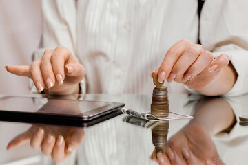 A woman counts finances on a tablet holding a coin from a stack on a banknote 