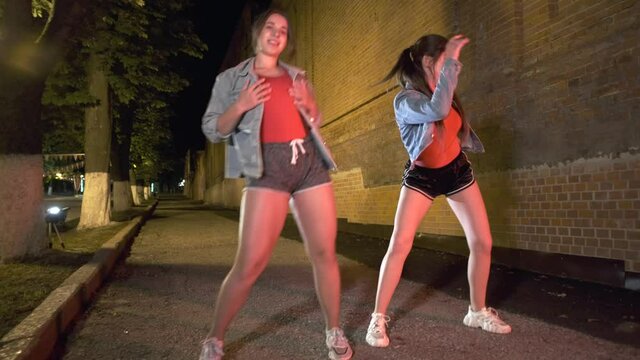 two young girls dance street dance in a city park in the evening. Youth subculture. Contemporary choreography. Gimbal shot