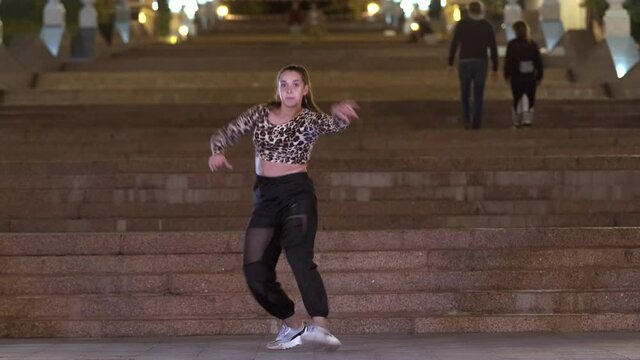 energetic young  woman in leopard t-shirt dancing street dance outdoors in front of an old huge stone staircase in night. Contemporary choreography