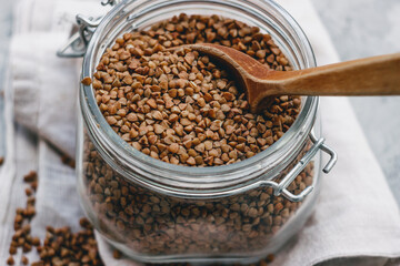 buckwheat in a glass jar with a wooden spoon, on a gray light background. Space for text, copy space