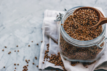 buckwheat in a glass jar with a wooden spoon, on a gray light background. Space for text, copy space