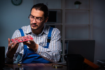 Young male technician repairing computer in workshop at night