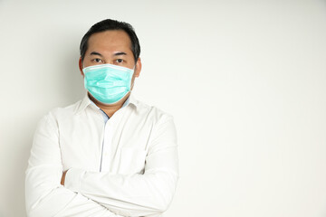 Asian man looks self-confident wearing a white shirt folds arms, wearing a medical mask to prevent the virus or dust entering the body isolated on white background. With copy space on right-hand side