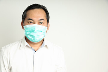 Asian man looks self-confident wearing a white shirt, wearing a medical mask to prevent the virus or dust looking at the camera isolated on a white background. With copy space on the right-hand side
