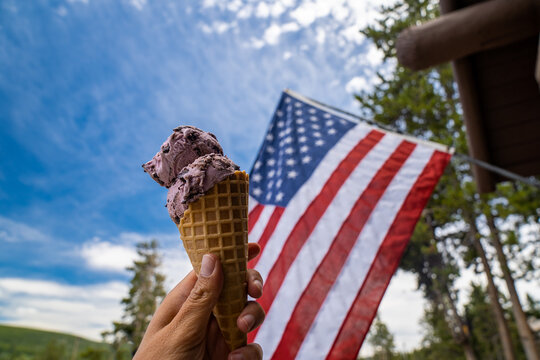 Woman hand holds a waffle cone ice cream with an American flag blowing in the background. Patriotic photo