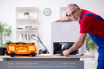 Old male contractor repairing refrigerator indoors